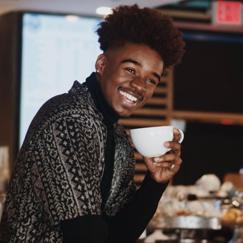 young man smiles while holding a cup of coffee in coffee shop
